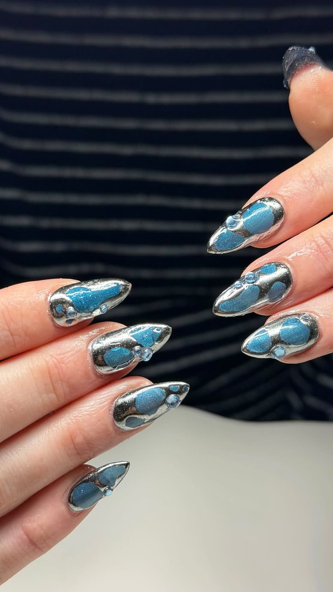 Chrome silver almond nails with blue marble inlay and gem accents